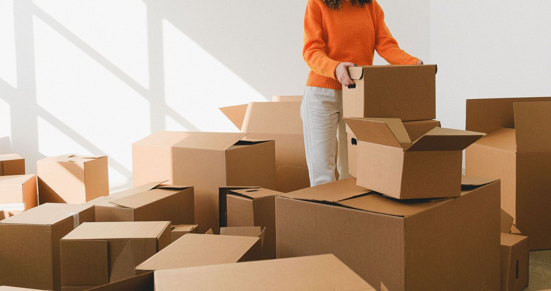 Focused young female with curly dark hair in casual outfit arranging pile of cardboard boxes while preparing for relocation in new apartment