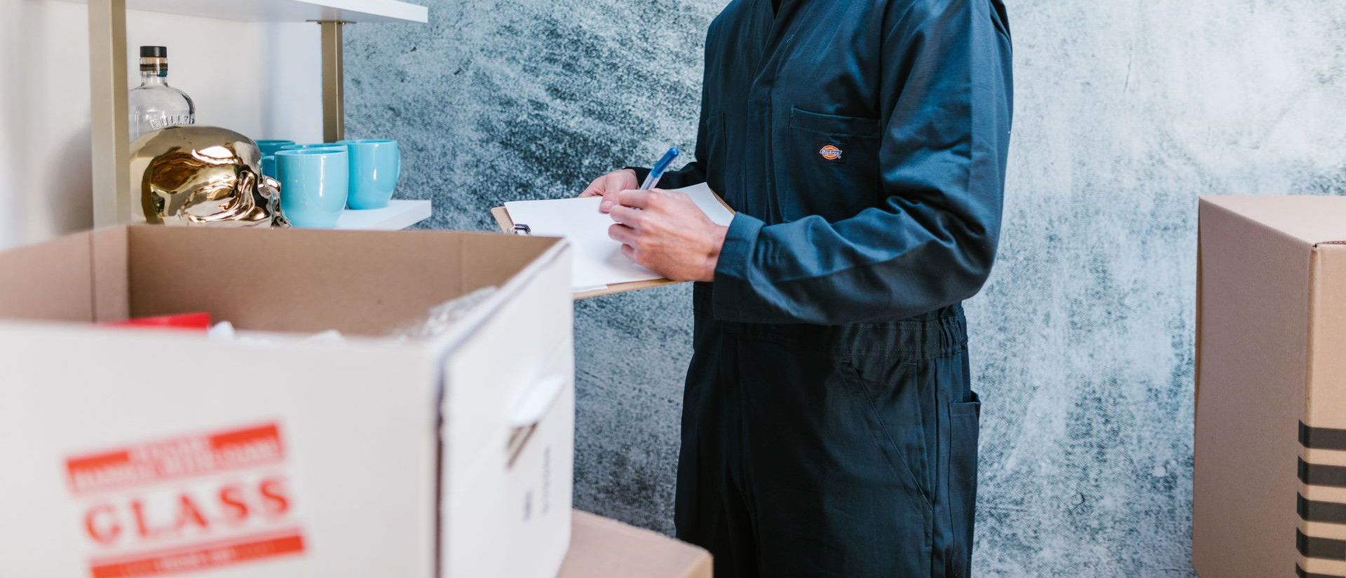 Man wearing overalls and bandana preparing for a home move, surrounded by boxes and fragile items.