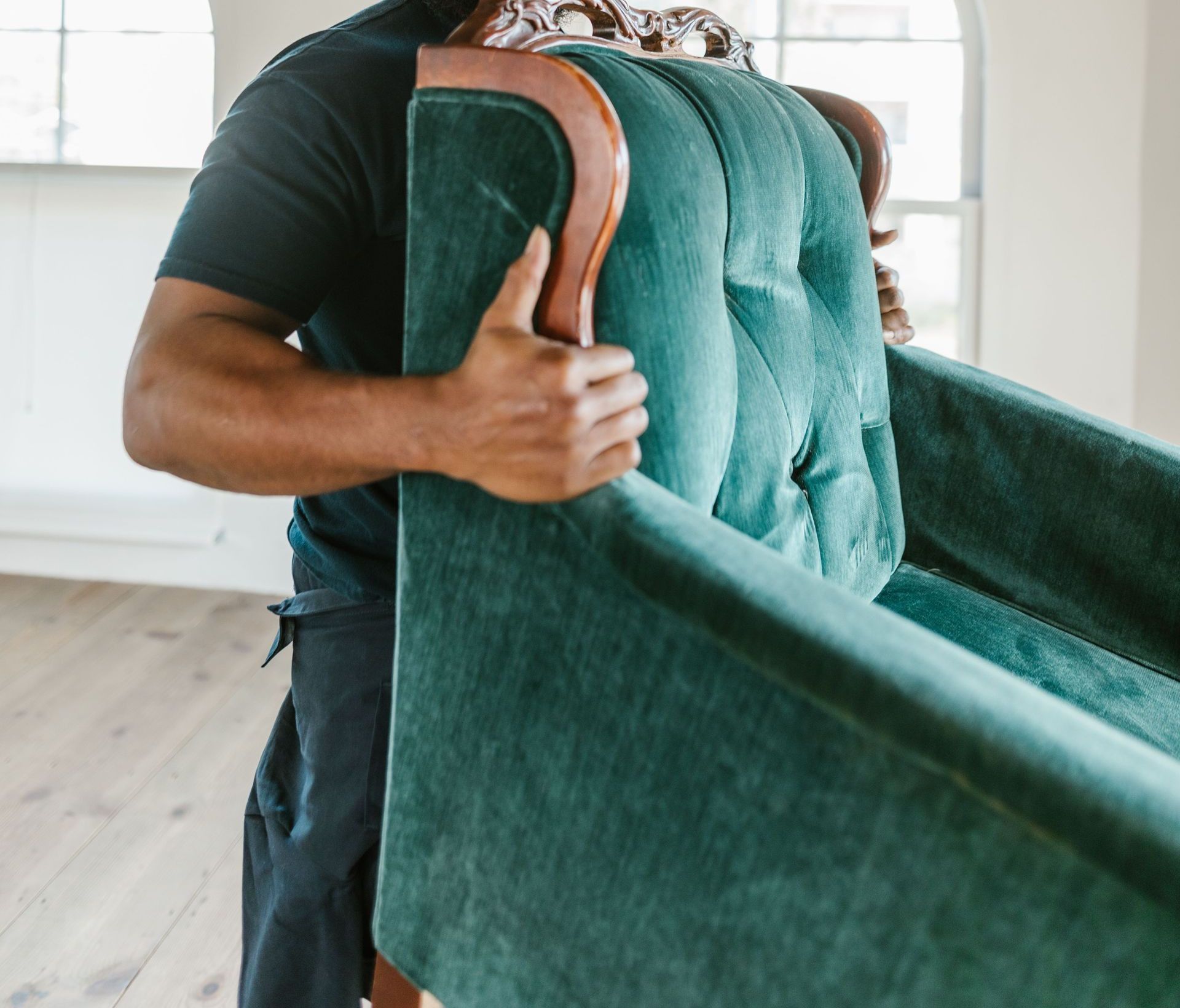 Man in a bright room moving a vintage green armchair with smile.