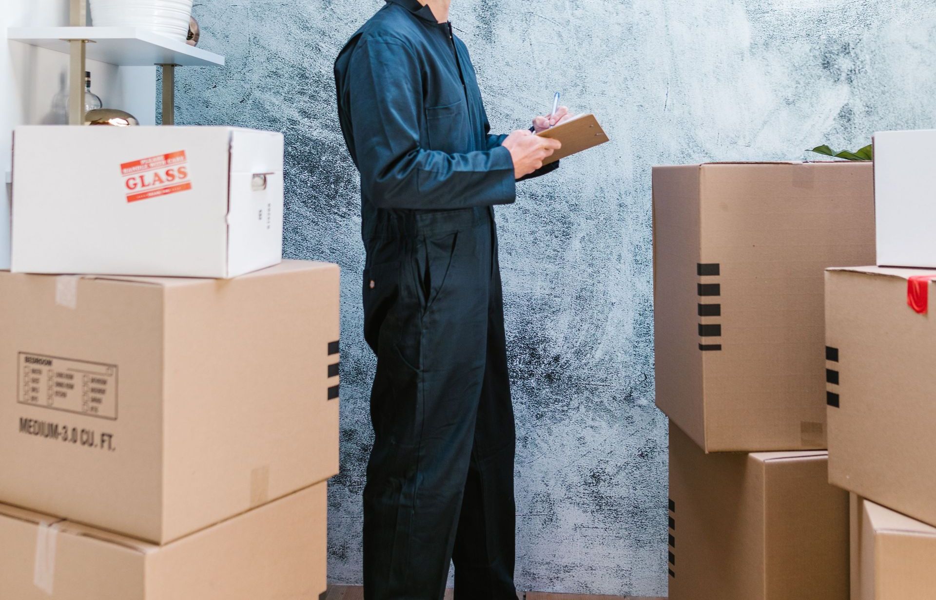 A mover in coveralls with bandana checks packages in a warehouse.